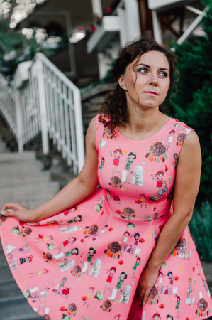 Beautiful brunette girl posing in pink dress outside near tropical plantsの写真素材