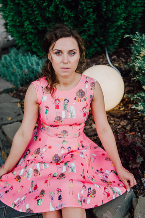 Beautiful brunette girl posing in pink dress outside near tropical plantsの写真素材
