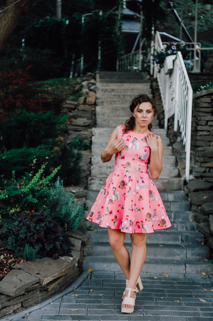 Beautiful brunette girl posing in pink dress outside near tropical plantsの写真素材