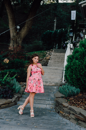 Beautiful brunette girl posing in pink dress outside near tropical plantsの写真素材
