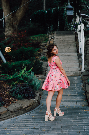 Beautiful brunette girl posing in pink dress outside near tropical plantsの写真素材