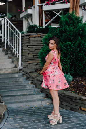 Beautiful brunette girl posing in pink dress outside near tropical plantsの写真素材