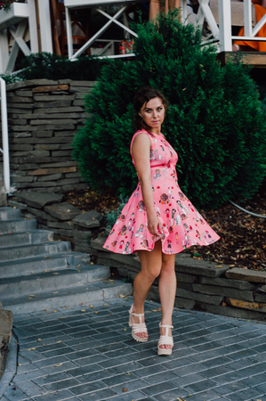 Beautiful brunette girl posing in pink dress outside near tropical plantsの写真素材