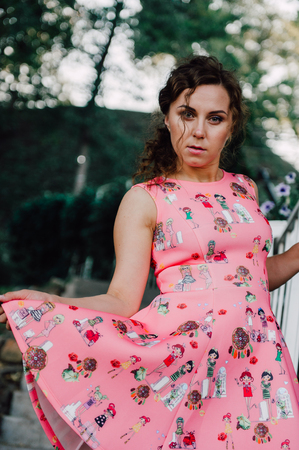 Beautiful brunette girl posing in pink dress outside near tropical plantsの写真素材