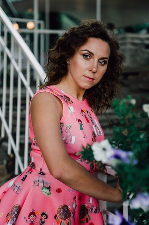 Beautiful brunette girl posing in pink dress outside near tropical plantsの写真素材