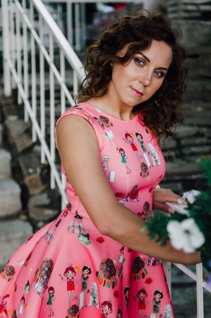 Beautiful brunette girl posing in pink dress outside near tropical plantsの写真素材