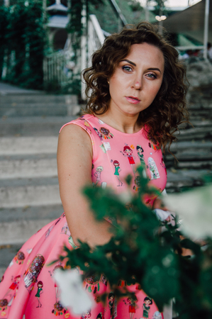 Beautiful brunette girl posing in pink dress outside near tropical plantsの写真素材