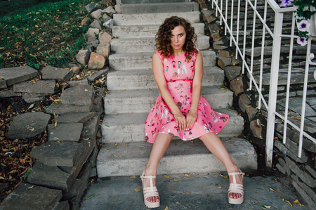 Beautiful brunette girl posing in pink dress outside near tropical plantsの写真素材
