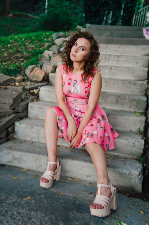 Beautiful brunette girl posing in pink dress outside near tropical plantsの写真素材