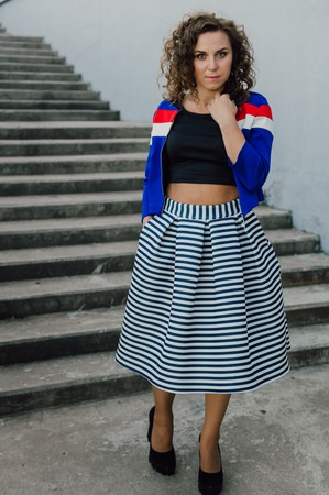 Beautiful sexy young brunette girl with long wavy hair thin slender figure and pretty face make-up wearing a long stripped skirt and black top, high heels. Walk on the street in casual styleの写真素材