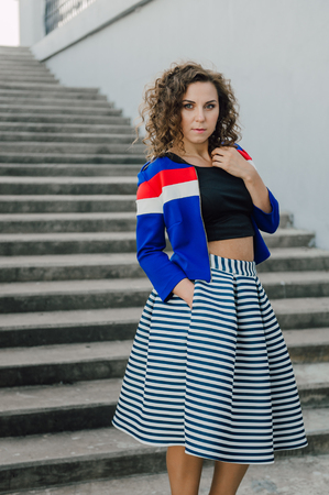 Beautiful sexy young brunette girl with long wavy hair thin slender figure and pretty face make-up wearing a long stripped skirt and black top, high heels. Walk on the street in casual styleの写真素材