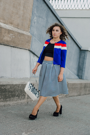 Beautiful sexy young brunette girl with long wavy hair thin slender figure and pretty face make-up wearing a long stripped skirt and black top, high heels. Walk on the street in casual styleの写真素材