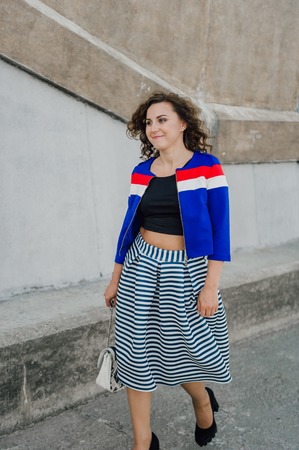Beautiful sexy young brunette girl with long wavy hair thin slender figure and pretty face make-up wearing a long stripped skirt and black top, high heels. Walk on the street in casual styleの写真素材