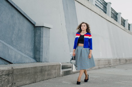 Beautiful sexy young brunette girl with long wavy hair thin slender figure and pretty face make-up wearing a long stripped skirt and black top, high heels. Walk on the street in casual styleの写真素材