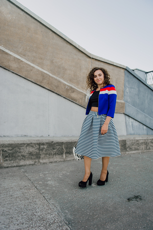 Beautiful sexy young brunette girl with long wavy hair thin slender figure and pretty face make-up wearing a long stripped skirt and black top, high heels. Walk on the street in casual styleの写真素材