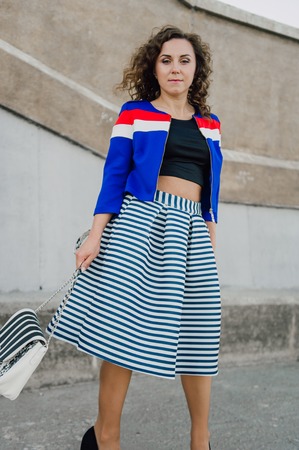 Beautiful sexy young brunette girl with long wavy hair thin slender figure and pretty face make-up wearing a long stripped skirt and black top, high heels. Walk on the street in casual styleの写真素材