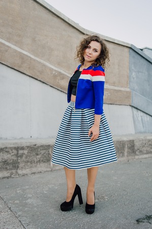Beautiful sexy young brunette girl with long wavy hair thin slender figure and pretty face make-up wearing a long stripped skirt and black top, high heels. Walk on the street in casual styleの写真素材
