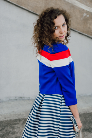 Beautiful sexy young brunette girl with long wavy hair thin slender figure and pretty face make-up wearing a long stripped skirt and black top, high heels. Walk on the street in casual styleの写真素材