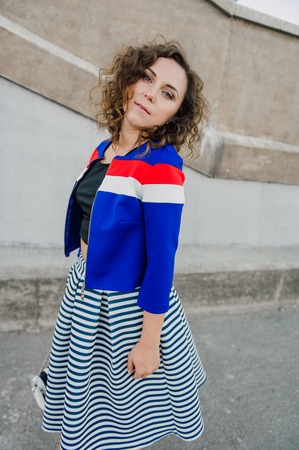 Beautiful sexy young brunette girl with long wavy hair thin slender figure and pretty face make-up wearing a long stripped skirt and black top, high heels. Walk on the street in casual styleの写真素材