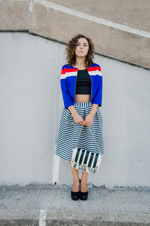 Beautiful sexy young brunette girl with long wavy hair thin slender figure and pretty face make-up wearing a long stripped skirt and black top, high heels. Walk on the street in casual styleの写真素材
