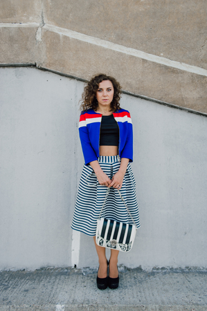 Beautiful sexy young brunette girl with long wavy hair thin slender figure and pretty face make-up wearing a long stripped skirt and black top, high heels. Walk on the street in casual styleの写真素材