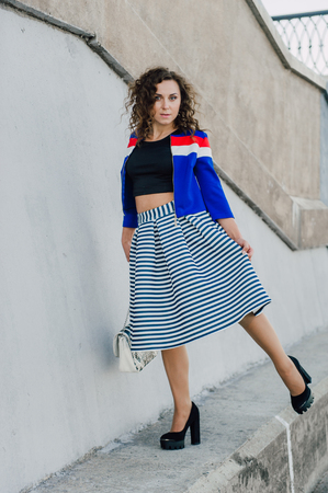 Beautiful sexy young brunette girl with long wavy hair thin slender figure and pretty face make-up wearing a long stripped skirt and black top, high heels. Walk on the street in casual styleの写真素材