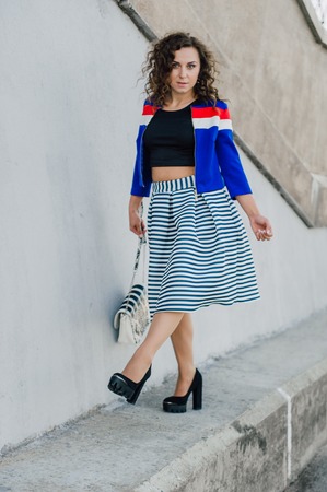 Beautiful sexy young brunette girl with long wavy hair thin slender figure and pretty face make-up wearing a long stripped skirt and black top, high heels. Walk on the street in casual styleの写真素材