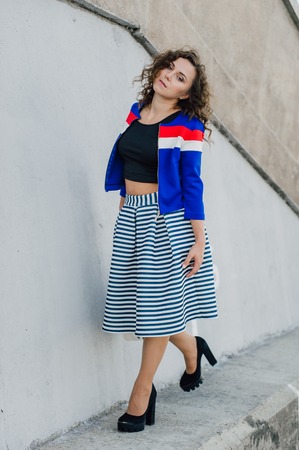 Beautiful sexy young brunette girl with long wavy hair thin slender figure and pretty face make-up wearing a long stripped skirt and black top, high heels. Walk on the street in casual styleの写真素材