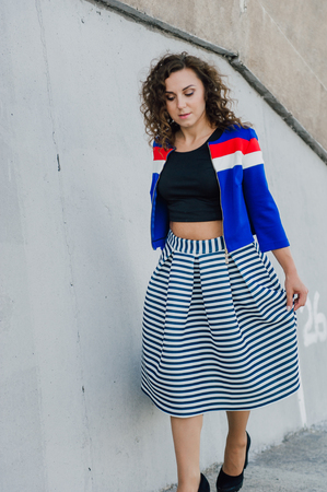 Beautiful sexy young brunette girl with long wavy hair thin slender figure and pretty face make-up wearing a long stripped skirt and black top, high heels. Walk on the street in casual styleの写真素材