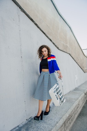 Beautiful sexy young brunette girl with long wavy hair thin slender figure and pretty face make-up wearing a long stripped skirt and black top, high heels. Walk on the street in casual styleの写真素材