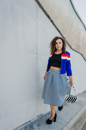 Beautiful sexy young brunette girl with long wavy hair thin slender figure and pretty face make-up wearing a long stripped skirt and black top, high heels. Walk on the street in casual styleの写真素材