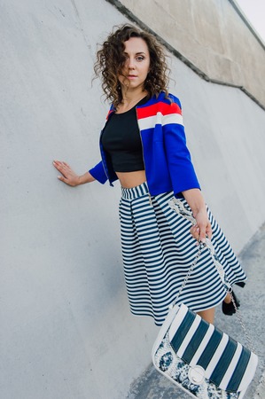 Beautiful sexy young brunette girl with long wavy hair thin slender figure and pretty face make-up wearing a long stripped skirt and black top, high heels. Walk on the street in casual styleの写真素材
