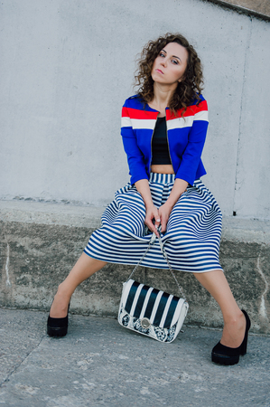 Beautiful sexy young brunette girl with long wavy hair thin slender figure and pretty face make-up wearing a long stripped skirt and black top, high heels. Walk on the street in casual styleの写真素材