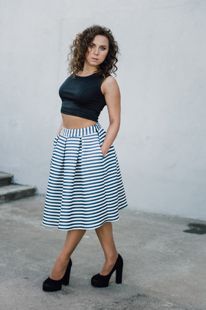 Beautiful sexy young brunette girl with long wavy hair thin slender figure and pretty face make-up wearing a long stripped skirt and black top, high heels. Walk on the street in casual styleの写真素材