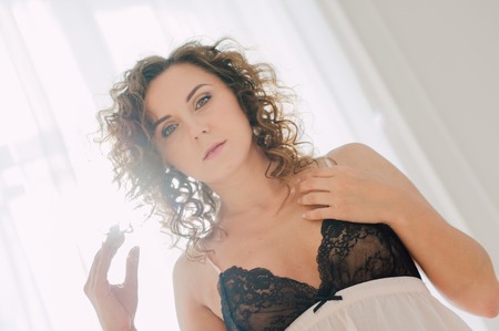 Sexy woman in bed in the morning showing her beautiful body. She doesn't wants to wake up. Awaken with natural light in her bedroom and covered with the bed sheets.の写真素材