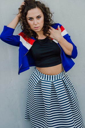 Beautiful sexy young brunette girl with long wavy hair thin slender figure and pretty face make-up wearing a long stripped skirt and black top, high heels. Walk on the street in casual styleの写真素材