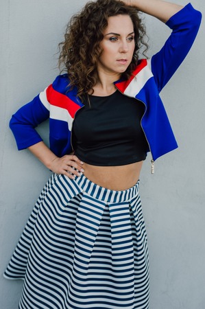 Beautiful sexy young brunette girl with long wavy hair thin slender figure and pretty face make-up wearing a long stripped skirt and black top, high heels. Walk on the street in casual styleの写真素材