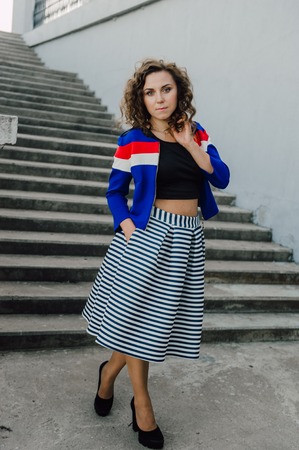 Beautiful sexy young brunette girl with long wavy hair thin slender figure and pretty face make-up wearing a long stripped skirt and black top, high heels. Walk on the street in casual styleの写真素材