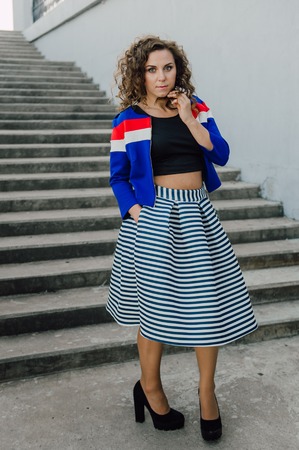 Beautiful sexy young brunette girl with long wavy hair thin slender figure and pretty face make-up wearing a long stripped skirt and black top, high heels. Walk on the street in casual styleの写真素材