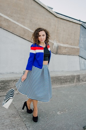 Beautiful sexy young brunette girl with long wavy hair thin slender figure and pretty face make-up wearing a long stripped skirt and black top, high heels. Walk on the street in casual styleの写真素材