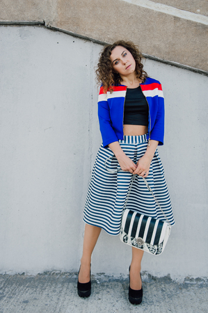 Beautiful sexy young brunette girl with long wavy hair thin slender figure and pretty face make-up wearing a long stripped skirt and black top, high heels. Walk on the street in casual styleの写真素材