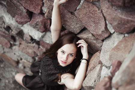 beautiful sad young woman on a stone wall background posing in a black dress, very sensual and emotionalの写真素材