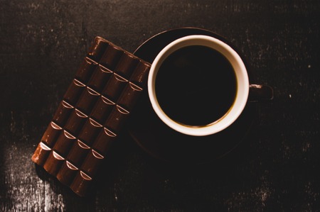 Cup of coffee with grains and chocolate on wooden table on dark backgroundの写真素材