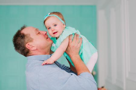 Portrait of a grandfather wearing blue  shirt with his small pretty granddaughter hugging him and listening attentively, studio shotの写真素材