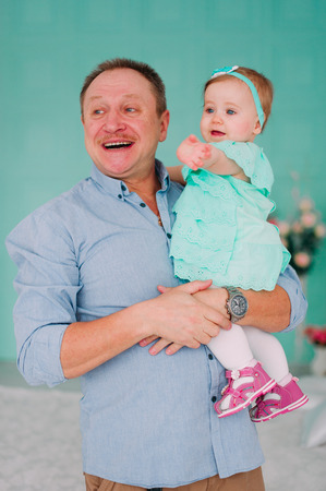 Portrait of a grandfather wearing blue  shirt with his small pretty granddaughter hugging him and listening attentively, studio shotの写真素材