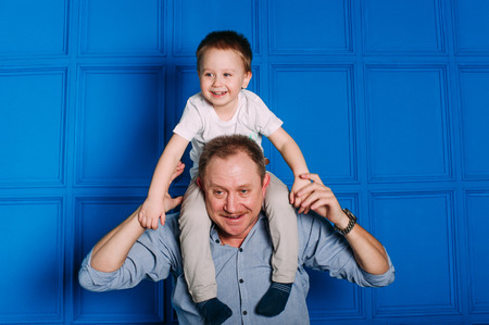 Laughing grandfather with his grandson as they play together indoors in the living room with the cute young boy hugging him from behindの写真素材