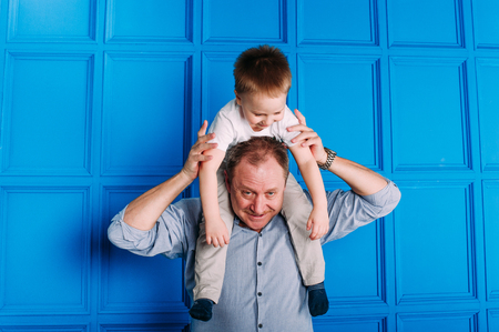 Laughing grandfather with his grandson as they play together indoors in the living room with the cute young boy hugging him from behindの写真素材
