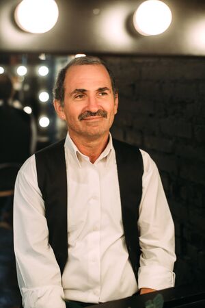 Handsome middle aged man is dressed in a white shirt and a black vest. Black background.