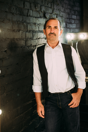 Handsome middle aged man is dressed in a white shirt and a black vest. Black background.の写真素材