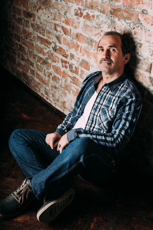 Handsome middle aged man is dressed in a white shirt and a black vest. Black background.の写真素材